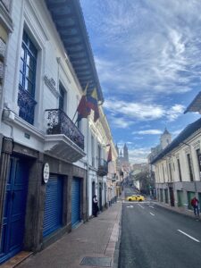 This is a photo of the streets of Quito, Ecuador, showcasing the colonial architecture and a flag of Ecuador