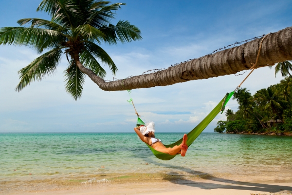 Person relaxing in hammock attached to curved palm tree over tropical beach