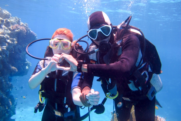 Two scuba divers underwater making hand signals near coral reef