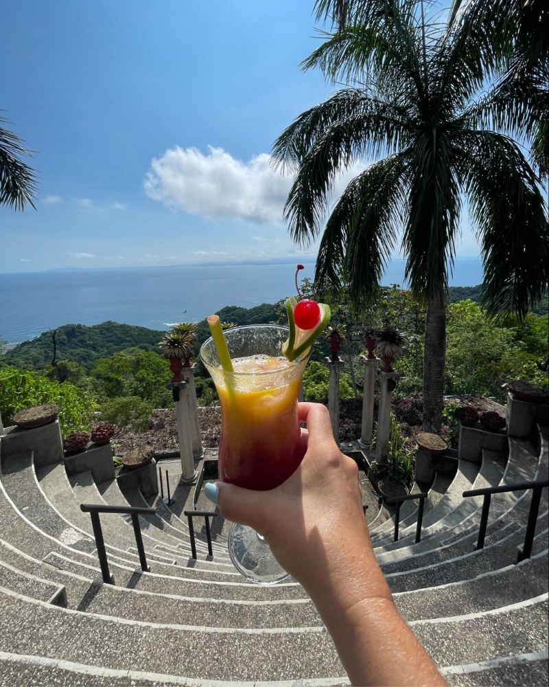 Layered tropical cocktail held up against amphitheater steps and Costa Rican coastal scenery