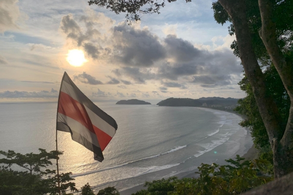 Costa Rican flag waving during sunset over curved beach bay with mountains